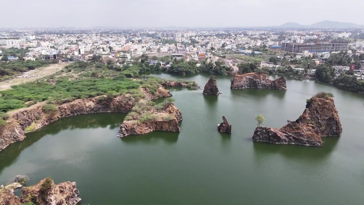 Ripresa drone che cattura scogliere di granito aspre, laghi di cava allagati e isole rocciose in una cava di granito di una città indiana. Acque verdi calme e lo sviluppo urbano circostante creano una sorprendente fusione naturale.