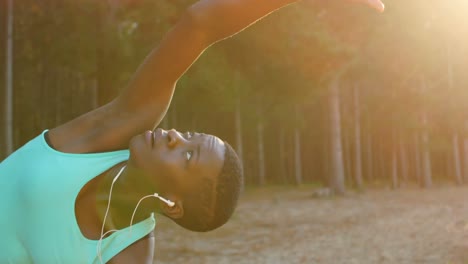 Female-athlete-performing-stretching-exercise-while-listening-music-in-forest-4k
