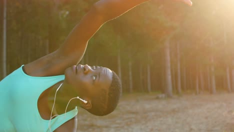 female athlete performing stretching exercise while listening music in forest 4k