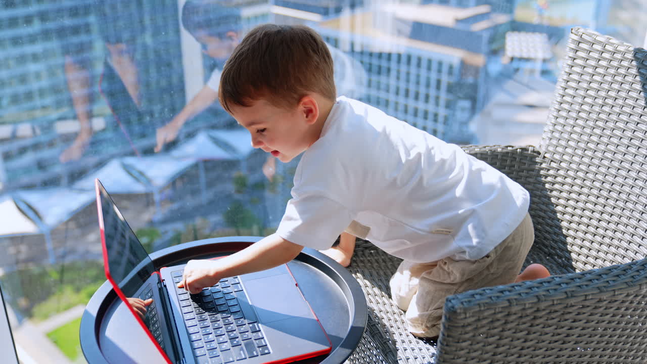 Boy plays with laptop at hotel. A young boy is happily interacting with a laptop while seated on a stylish chair