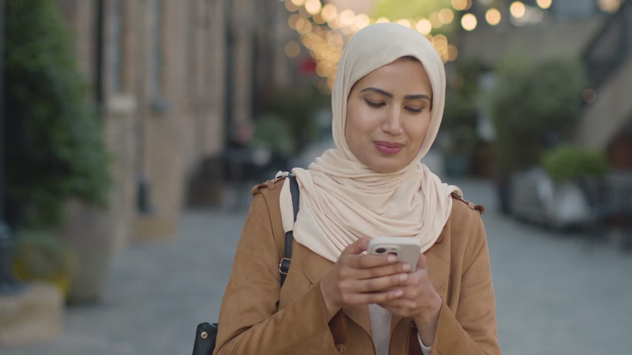 mujer musulmana con hijab caminando por la calle de la ciudad enviando un mensaje de texto hasta la fecha en el teléfono móvil 1