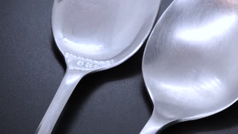 close up view of two steel spoons on a black bacground, rotating motion