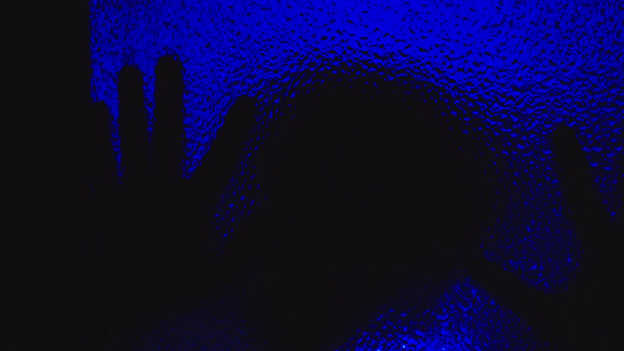 la escalofriante silueta de un hombre poseído se arrastra por el vidrio en la oscuridad bajo la inquietante luz azul.