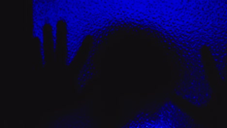 spine-chilling silhouette of possessed man creeps on glass in the dark under haunting blue light