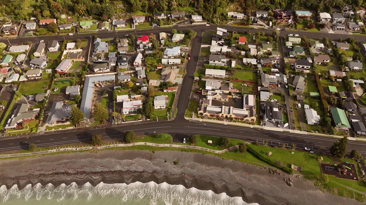 Coastal town of Kaikoura, sandy beach, ocean waves, and residential area on South Island, New Zealand. Aerial tilt-down