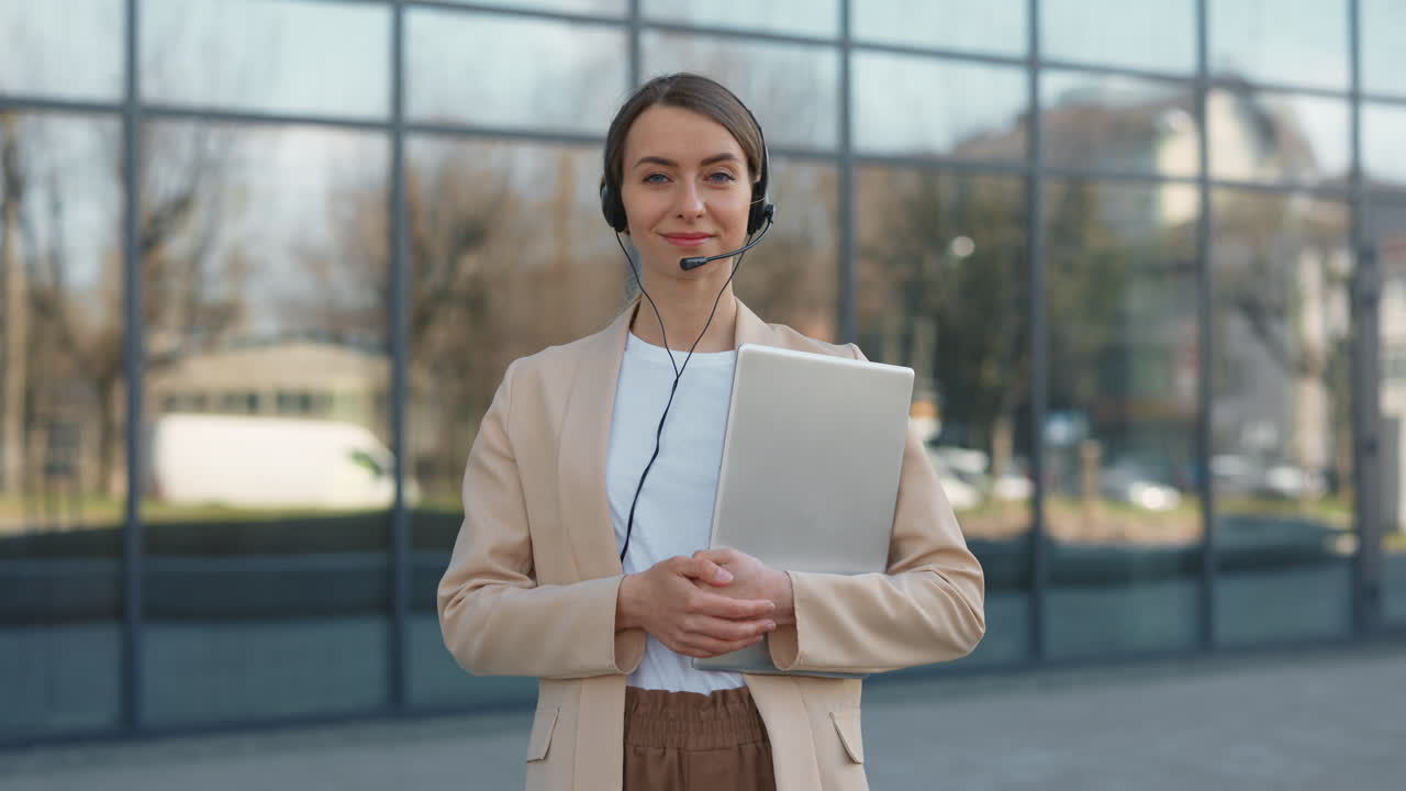 Ung kvinne med headset holder bærbar PC smilende til kamera