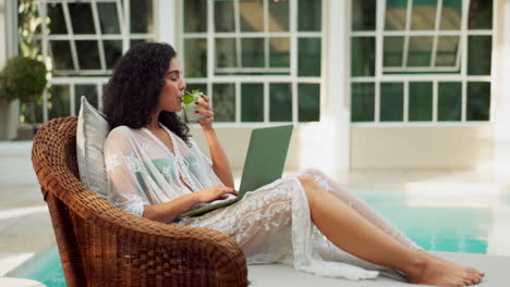 woman relaxing by the pool with laptop and drink