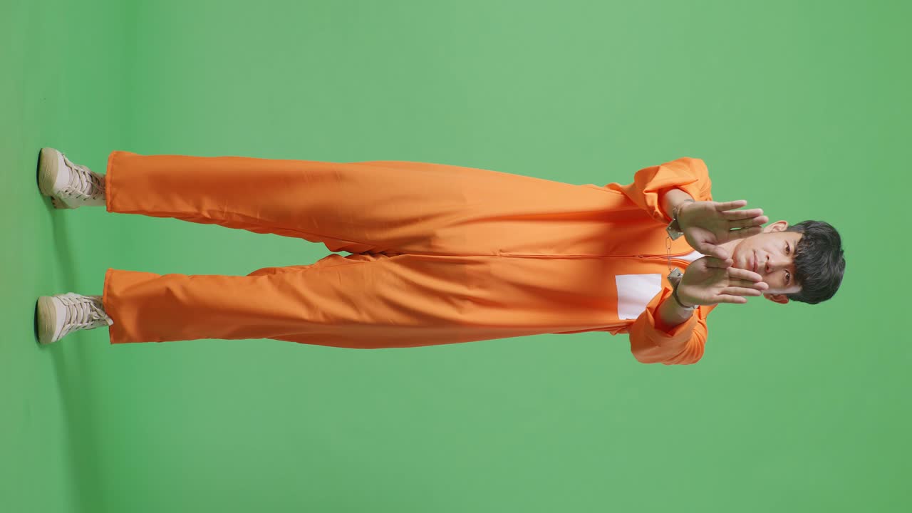 Full Body Of Asian Male Prisoner In Handcuffs Standing On The Green Screen Background, Shaking His Head And Showing Rejecting Gesture By Stop Palm Sign