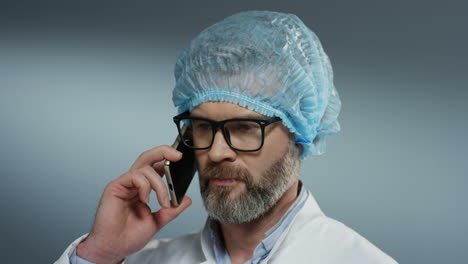 Nahaufnahme-Des-Wütenden-Arztes-Mit-Blauem-Hut-Und-Brille,-Der-Telefoniert-Und-Nach-Der-Operation-Etwas-Bestreitet