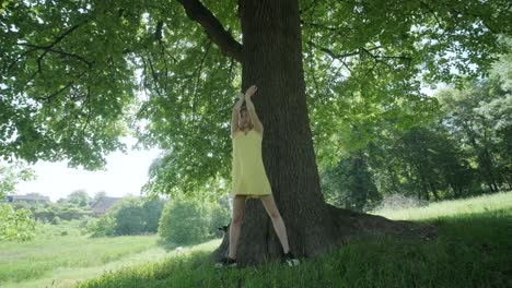 woman in yellow dress dancing by tree in summer park