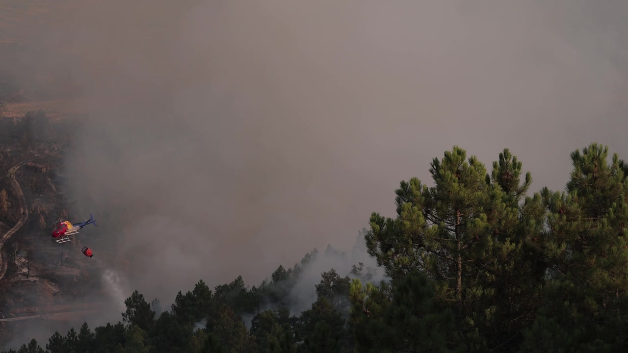 Elicottero Airbus H125 che sgancia acqua su un vasto incendio boschivo in Portogallo, con fumo denso, luce suggestiva e dettagli al rallentatore che intensificano l'urgente scena antincendio.