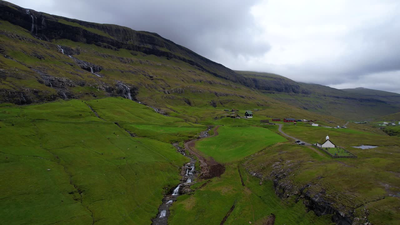 페로 제도 사크손 의 잔디 지붕 건물 을 둘러싸고 있는 푸른 화산 산 과 폭포