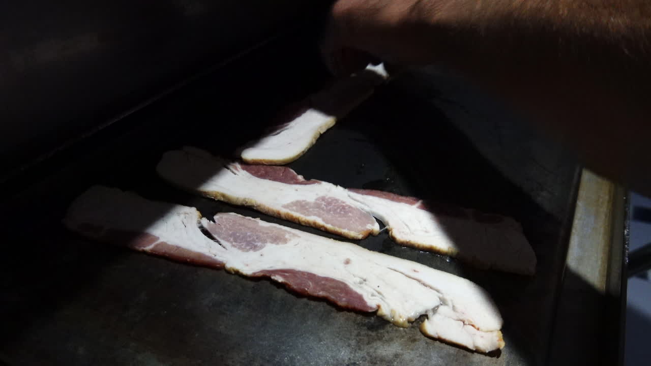 Close up shot of bacon being cooked on a griddle top on a boat