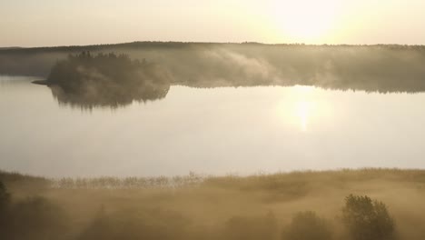 aerial: misty sunrise above scandinavian landscape with lake and forest