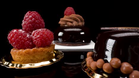 macro-view-moving-past-small-cakes-and-pastries-on-black-background