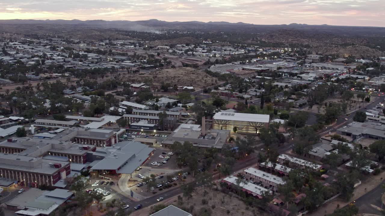 Sideways aerial footage of the township of Alice springs, Mparntwe, including the Alice Springs Hospital, at dusk, in the Northern Territory, Australia. August 2022.