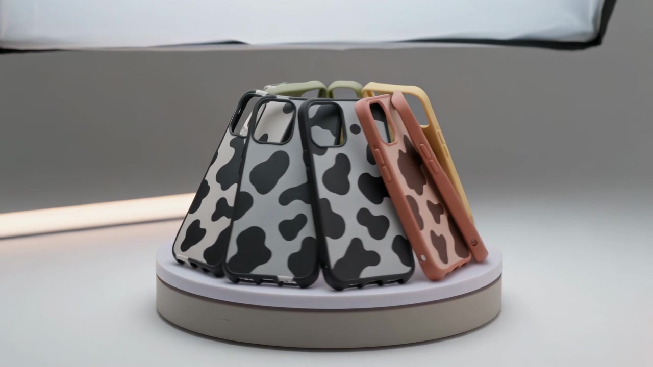 Une plateforme tournante présentant des coques de téléphone à motif vache pour une présentation de produit en studio, avec une boîte à lumière au-dessus.