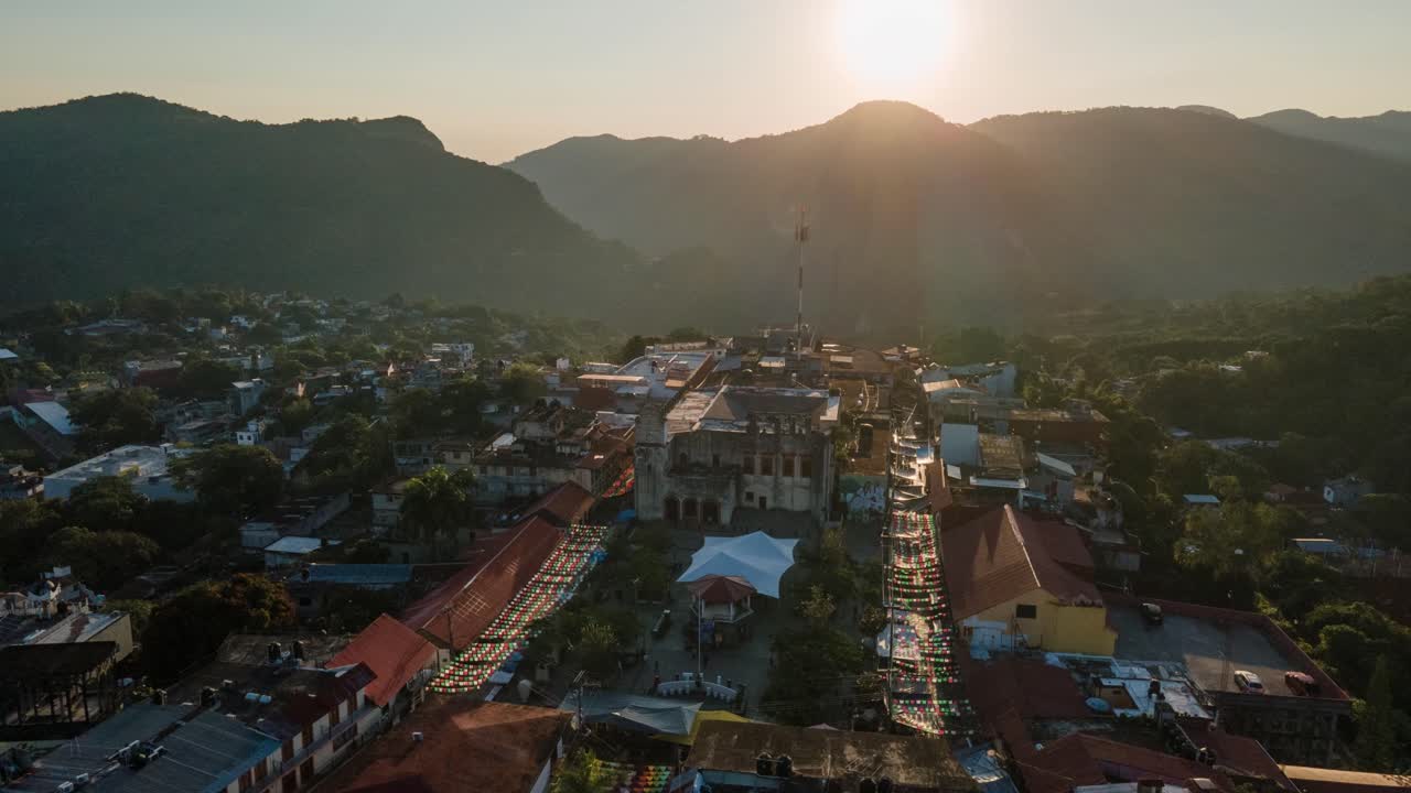 Vista aerea in hyperlapse orbitante della piazza nella città di Xilitla, con l'alba dietro le montagne sullo sfondo.