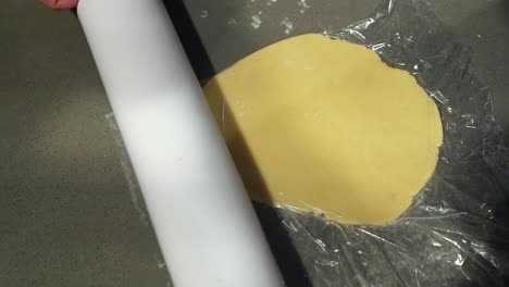 a rolling pin flattening a circle of sugar cookie dough from above in order to bake holiday christmas cookies on a cold winter night