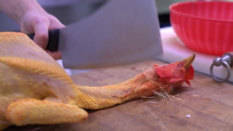 manos humanas cortando una cabeza de pollo antes de quemar el plumaje de una mesa de madera en la cocina