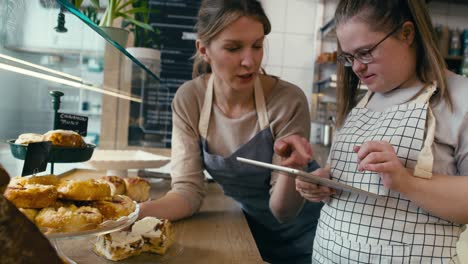 down syndrome girl and her female workmate using digital tablet to check the commodity of the bakery