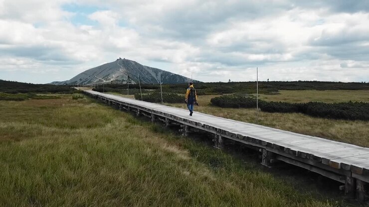 Escursionista solitario nella torbiera di Upa nei Monti Krkonoše o Monti dei Giganti, Repubblica Ceca, con il picco Snezka in lontananza. Drone in follow, 4k o UHD, 30fps.