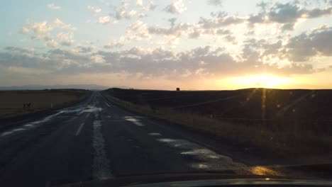 view from inside car on empty hilly road leading to horizon line at sunset or sunrise