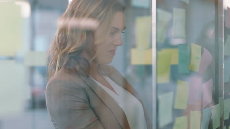 beautiful business woman using sticky notes brainstorming ideas on glass whiteboard smiling proud of successful solution planning strategy problem solving with creative mind map in office 4k