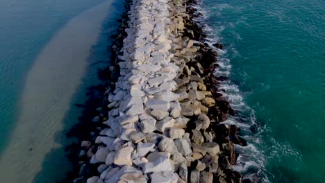 Aerial-dolly-over-rock-wall-jetty-separating-ocean-waves-from-harbor