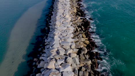 dolly aéreo sobre el embarcadero de la pared de roca que separa las olas del océano del puerto