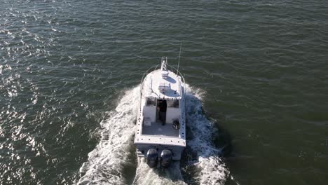 Una-Vista-Aérea-De-Un-Barco-De-Pesca-Que-Se-Dirige-Al-Mar,-Mientras-Un-Pescador-Prepara-Las-Cañas-De-Pescar