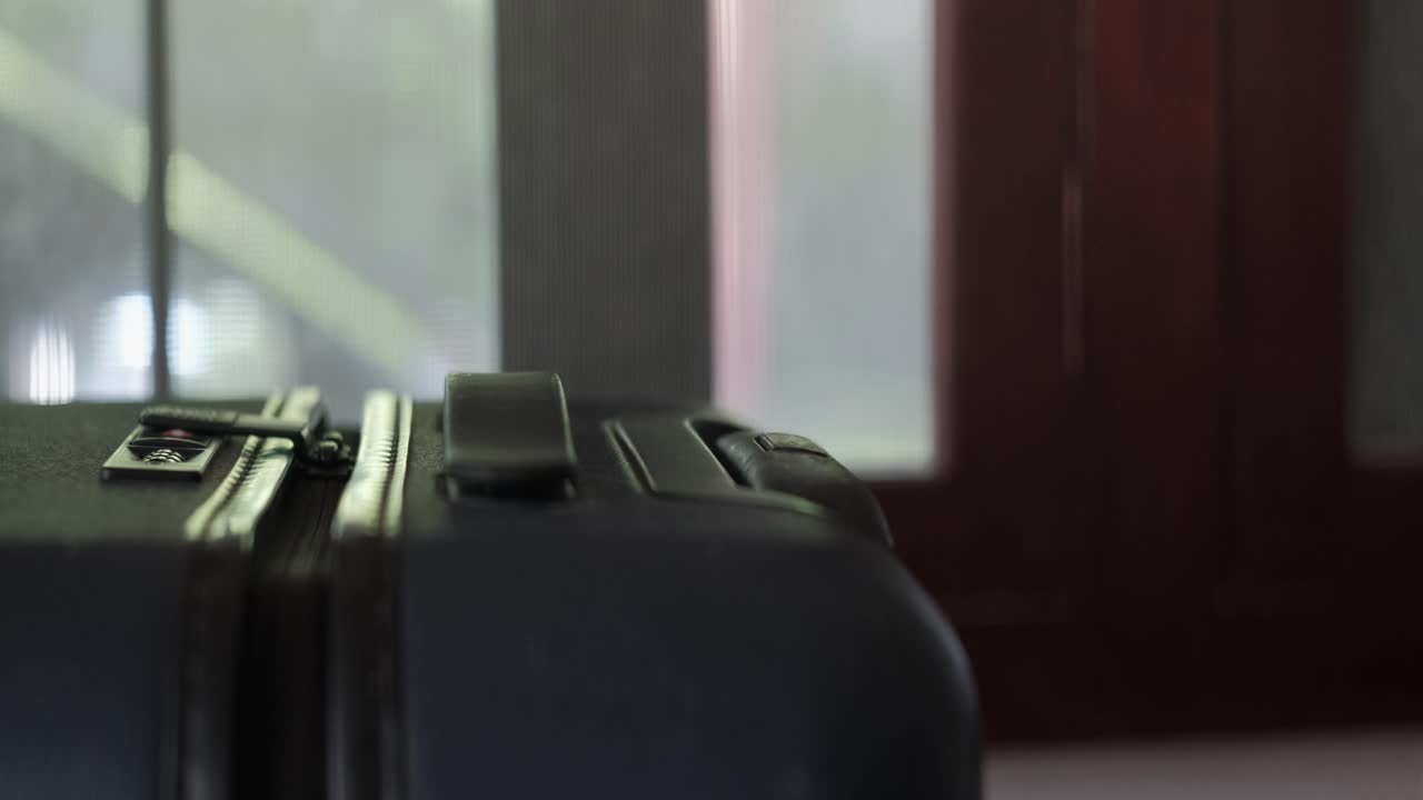 Close-up static shot of hand pulling up telescopic handle of black carry-on suitcase and rolling away
