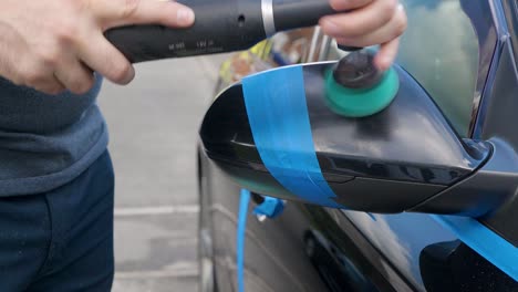 polishing a black car mirror with a small machine polisher