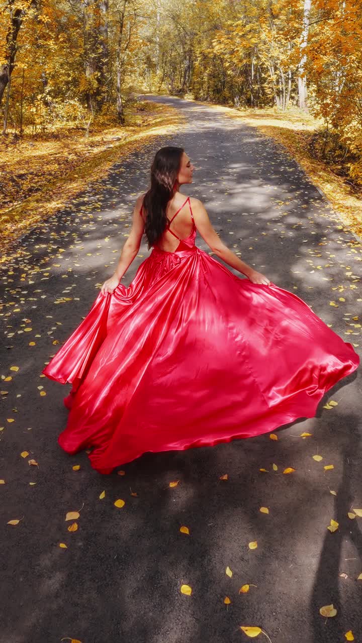 A Captivating Journey Through Autumn: A Woman in a Flowing Red Dress Walking Along a Leaf-Covered Road Surrounded by Vibrant Fall Foliage