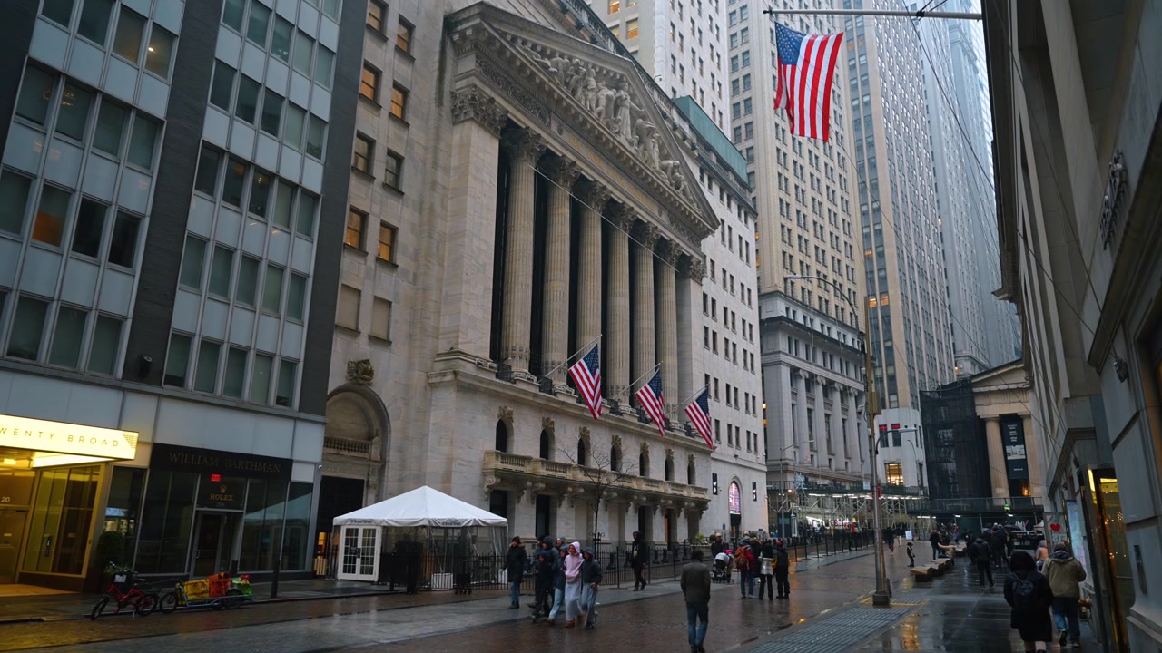 New York, USA, 25. december 2025: Klassisk facade af New York Stock Exchange på en overskyet Wall Street. Våd asfalt og klassiske søjler på NYSE-bygningen med vajende amerikanske flag i New York City.