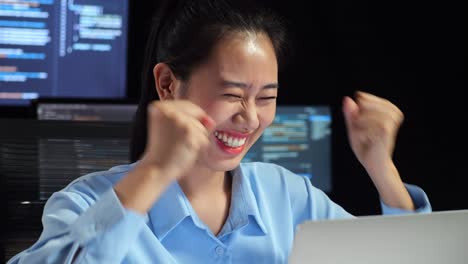 close up of asian female programmer celebrating succeed writing code by a laptop using multiple monitors showing database on terminal window desktops in the office