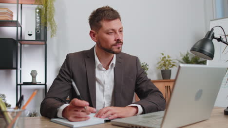 Businessman-lawyer-in-suit-working-on-laptop-online,-writing-notes-in-planner-notebook-at-office