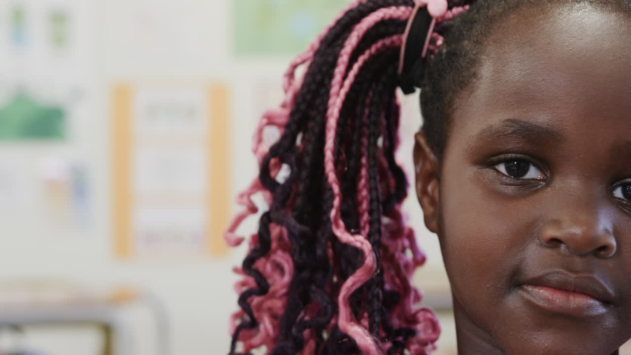 In school, young girl with colorful braids smiling peacefully in classroom, copy space