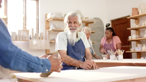 Focused-biracial-potter-with-long-beard-shaping-clay-with-hands-in-pottery-studio,-slow-motion