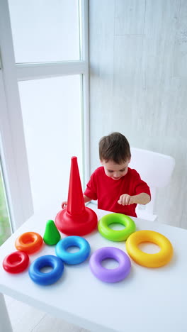 cheerful toddler boy sits at desk building a pyramid. top view on the baby busy with a construction game. vertical video.