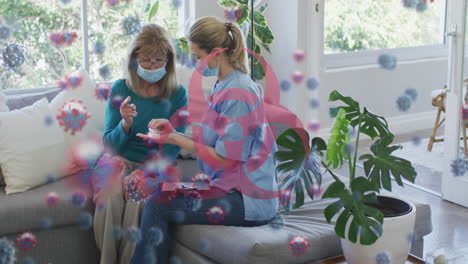 animation of virus cells and biohazard icon over caucasian senior woman and nurse wearing face masks