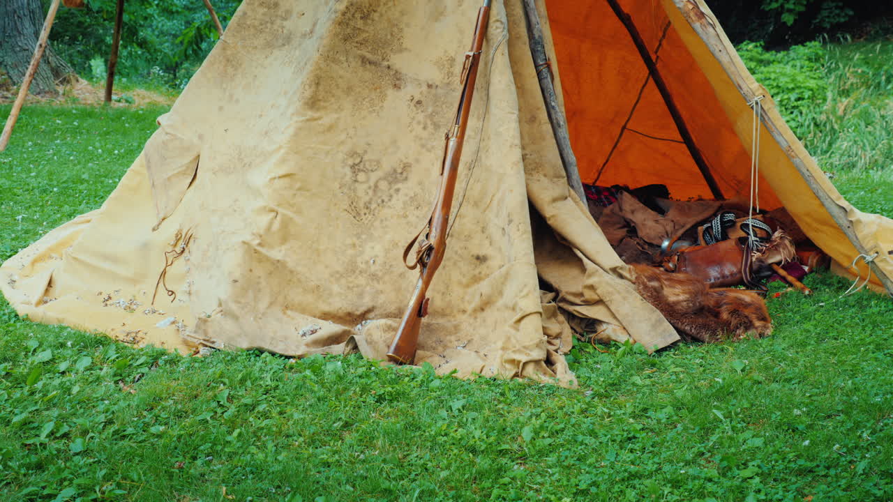 숲 속에 있는 오래된 사냥꾼의 천막에는 동물 가죽과 미국 개척자들의 무기가 놓여 있습니다.