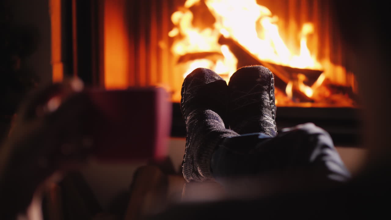 한 남자가 손에 차 한 잔을 들고 벽난로 옆에서 쉬고 있다