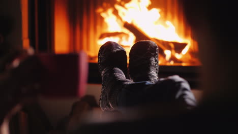 a man is resting by the fireplace holding a cup of tea in his hand only socks in the frame are visib