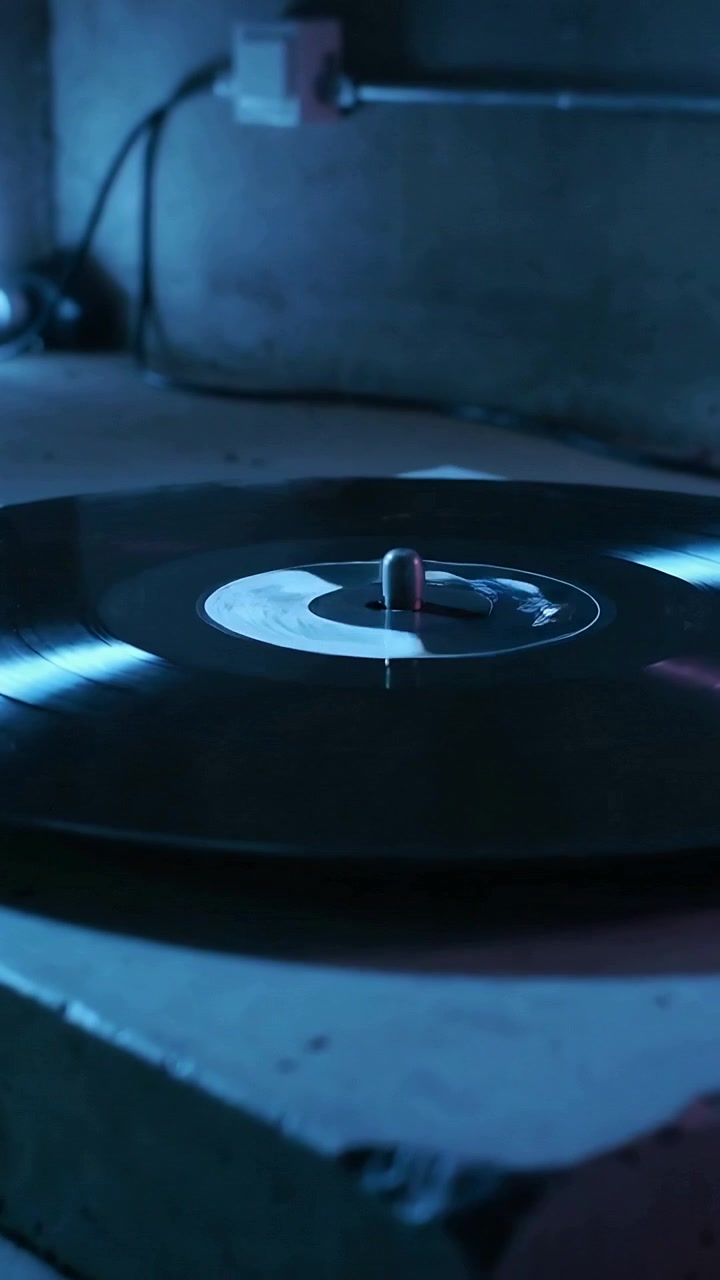 Video verticale: Vinile nero che gira sul perno nell'angolo di un seminterrato, lampada che proietta riflessi blu.