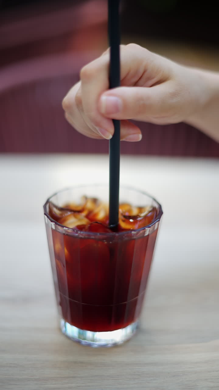 Close up of a woman mixing an iced coffee with a straw. Vertical