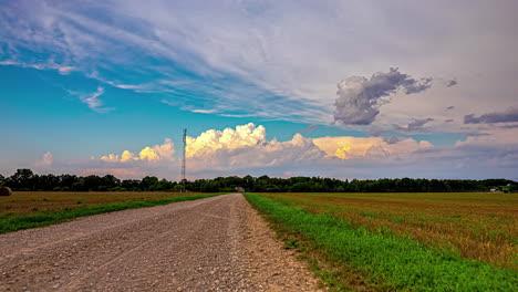 gravel road, green fields and vibrant cloudscape time lapse