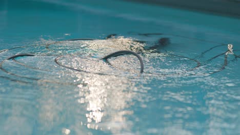 Elektrischer-Poolreinigungsroboter-Reinigt-Schwimmbad-Mit-Kabeln,-Die-In-Klarem,-Reflektierendem-Wasser-Schwimmen