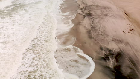 aerial shot of flying backwards looking down at waves breaking onto a sandy beach