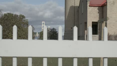 Old-Mackinac-Point-lighthouse-in-Mackinaw-City,-Michigan-with-white-picket-fence-in-foreground-and-Mackinac-Bridge-in-background-with-dolly-moving-right-to-left